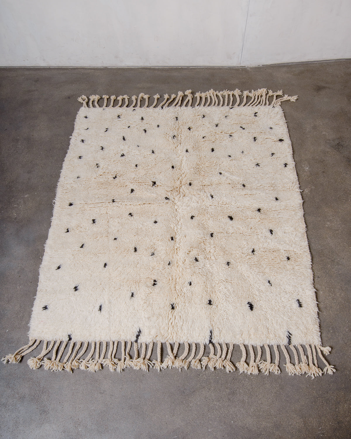 Berberlin Beniourain rug in cream wool with black dots laying on concrete floor.